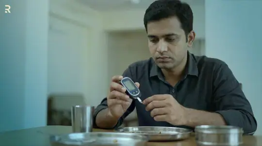 Indian man checking his blood sugar with a glucometer at the dining table, a daily step in managing diabetes-related erectile dysfunction