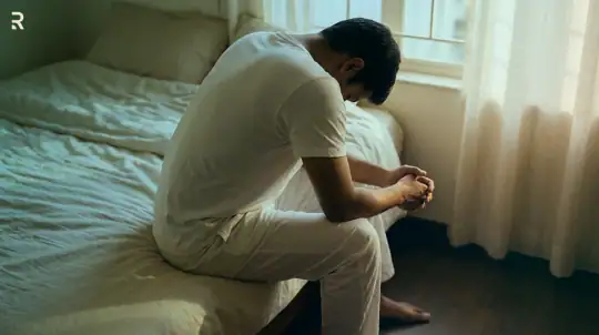 Worried young man sitting on the edge of his bed with his head down, anxious about a sexual health problem