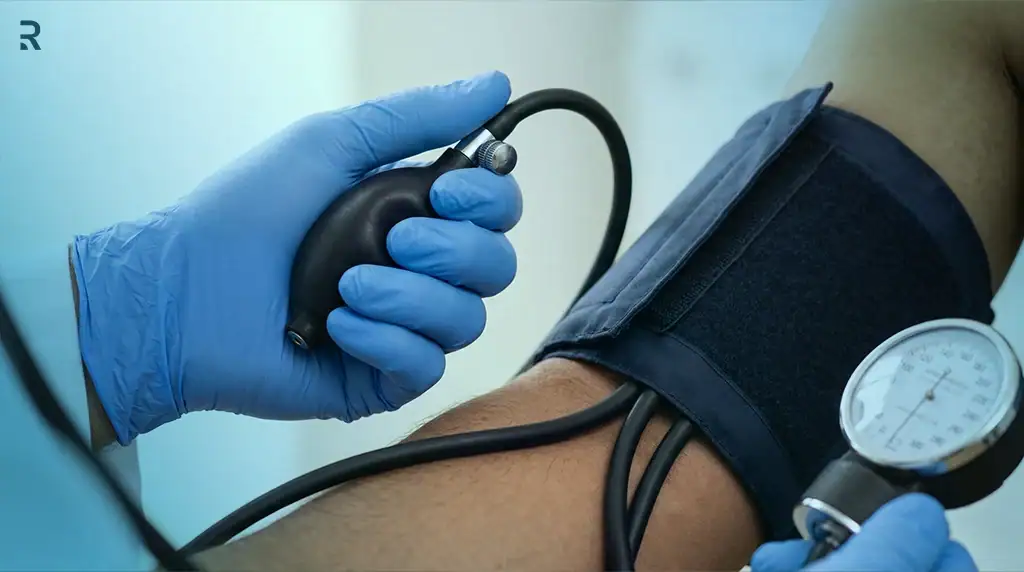 Doctor in blue gloves checking a man's blood pressure with an arm cuff and dial gauge