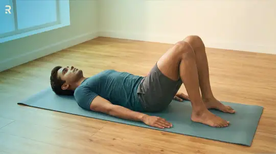 Man lying on his back on a yoga mat with his knees bent, doing Kegel pelvic floor exercises for premature ejaculation at home