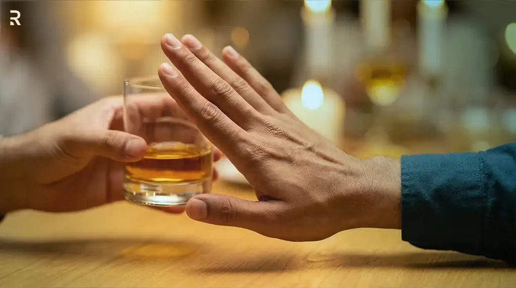 A man raises his hand to refuse a glass of whisky offered across a table, cutting down on alcohol to protect his erections