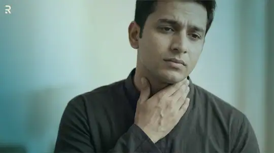 Worried Indian man touching the front of his neck where the thyroid gland sits